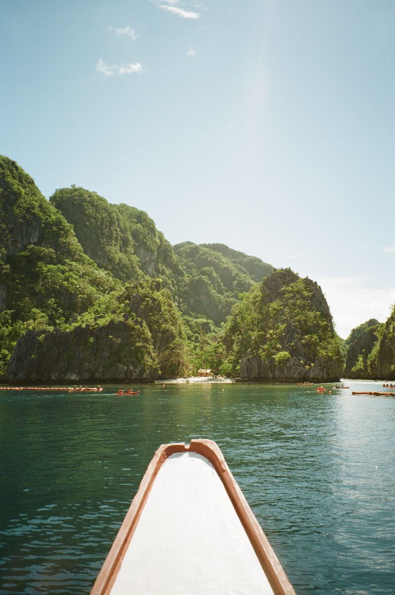 The bow of a boat pointing toward a lagoon flanked by limestone cliffs